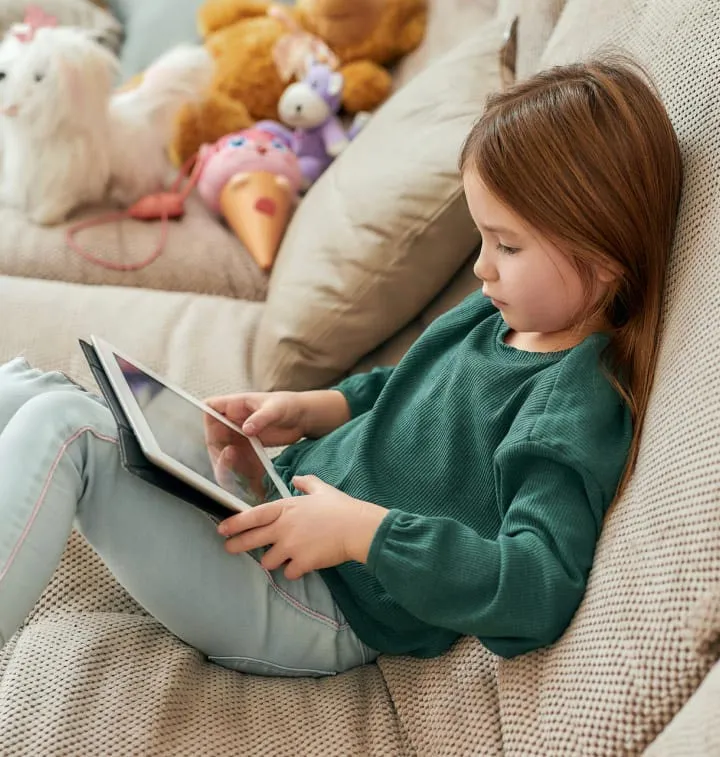 Petite fille assise sur un canapé avec une tablette sur les genous