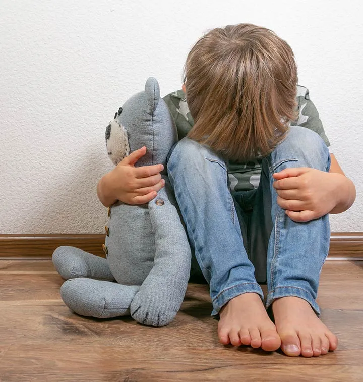 Enfant assis par terre la tête dans les genoux avec un doudou